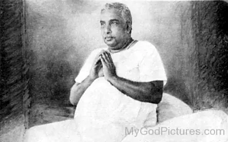 Sri Sri Thakur Anukulchandra in his later years, seated in a white kurta with his hands folded
