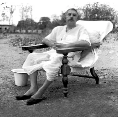 Sri Sri Thakur Anukulchandra in a white kurta and dhoti, resting in a wooden armchair in an open field