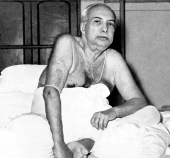 Sri Sri Thakur Anukulchandra in his later years, seated on his bed among white pillows