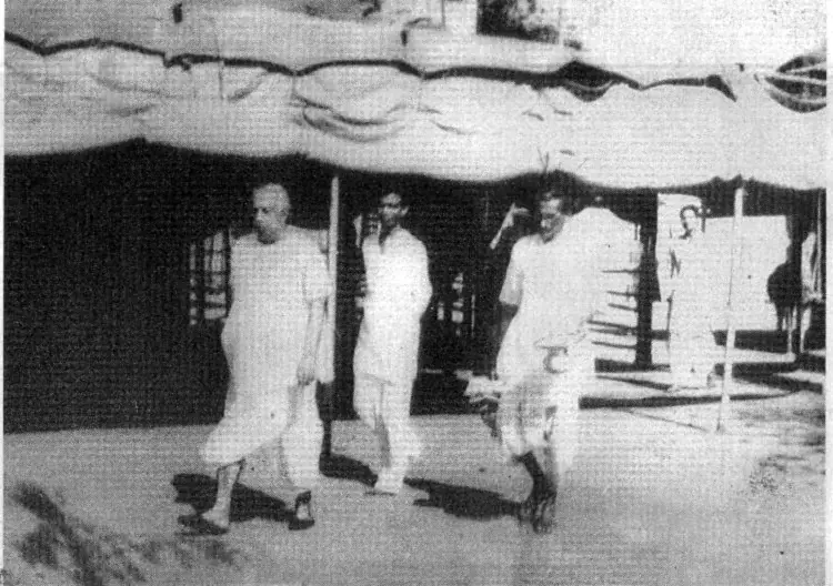 Sri Sri Thakur Anukulchandra walking with devotees under a canvas canopy towards Boral in Deoghar, 1951